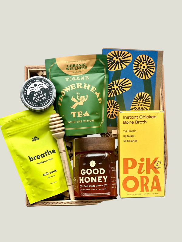 Collection of health and wellness products including tea, honey, and bone broth in a box on a gray background.