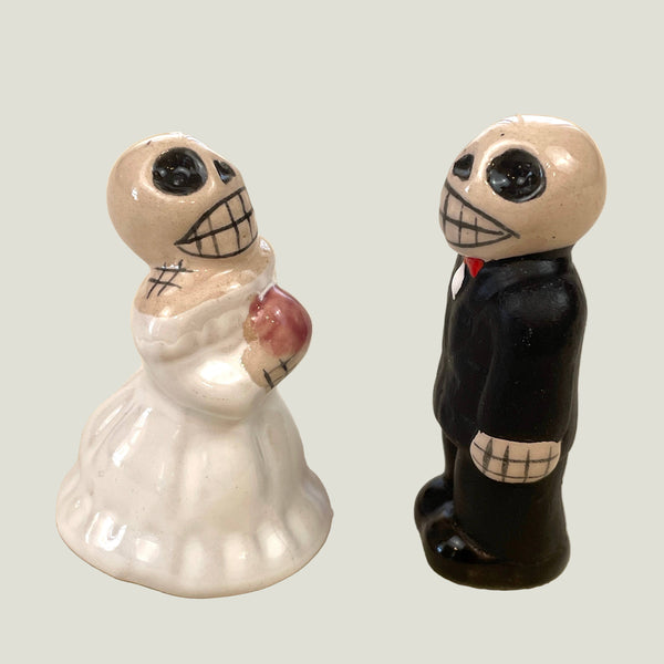Two ceramic figures of a bride and groom with skull designs on a beige background