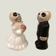 Two ceramic figures of a bride and groom with skull designs on a beige background