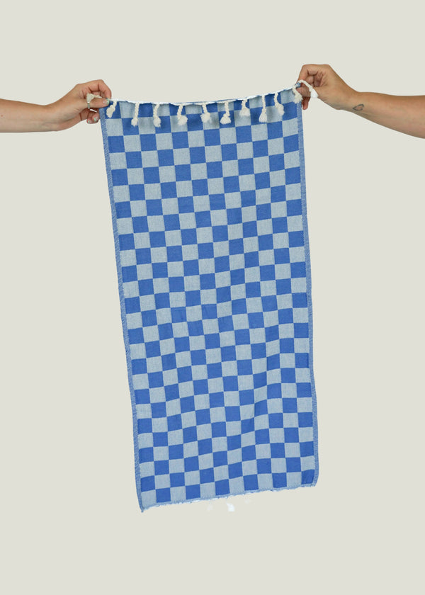 Two hands holding a blue and white checkered towel against an off-white background