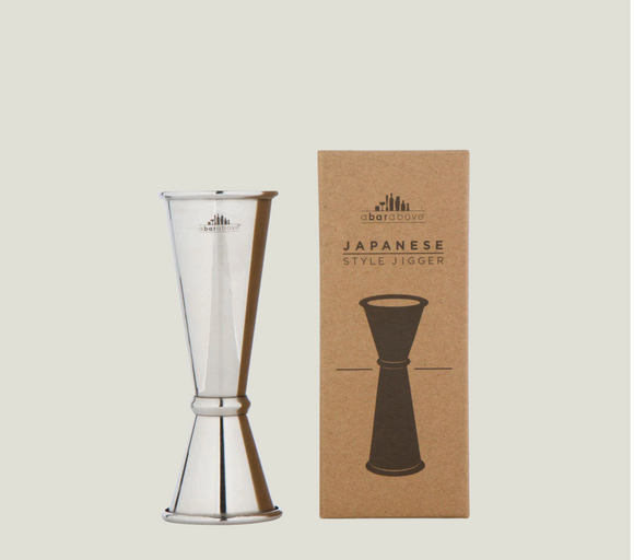 Clear glass Japanese style jigger and brown cardboard box with brand logo on a light beige background