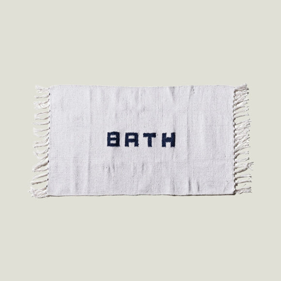 White bath mat with 'BATH' text and tassels on a white background