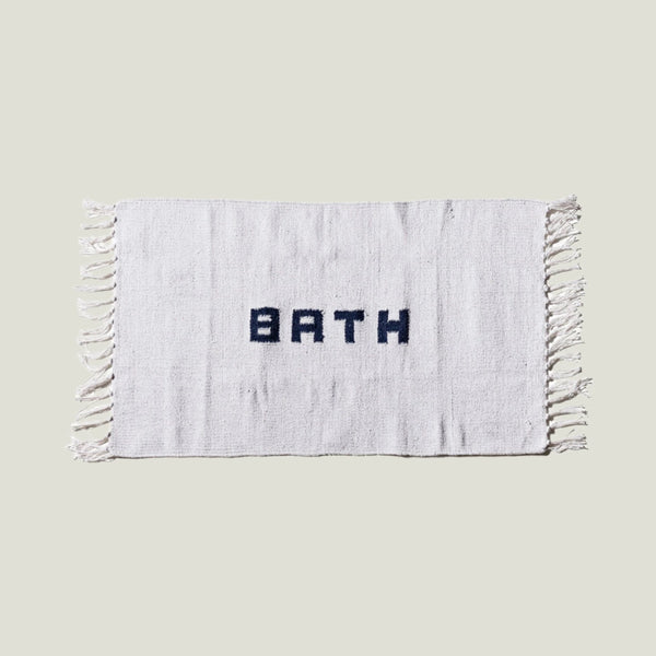 White bath mat with 'BATH' text and tassels on a white background