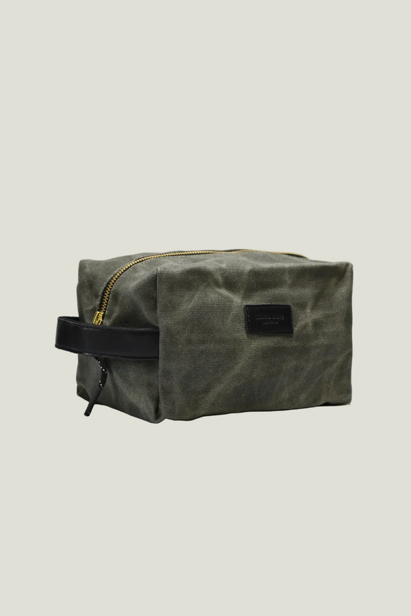 Green waxed canvas toiletry bag with black strap on a light gray background