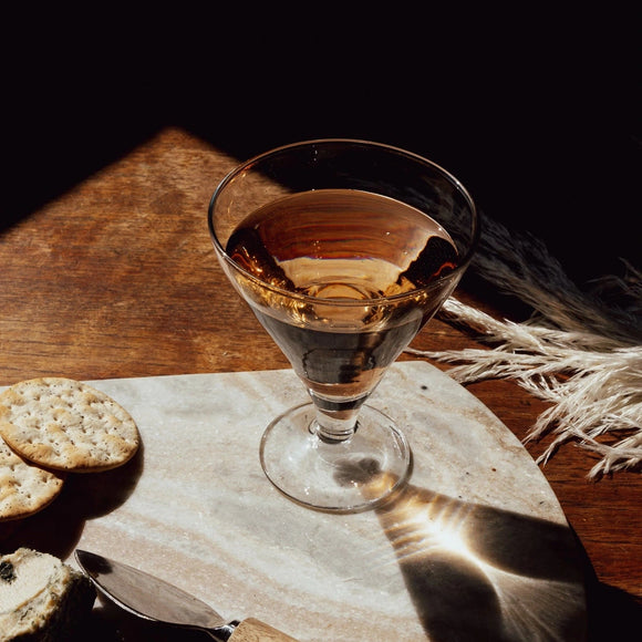 Glass of amber liquid on a wooden surface with crackers and a knife.