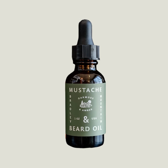 Bottle of Mustache & Beard Oil with a green label on a white background. Oakmoss and Amber scented.