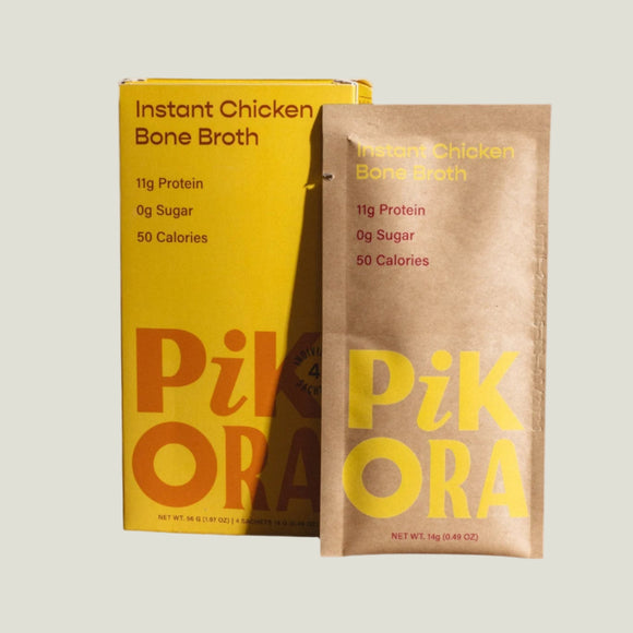 A packaged product labeled 'Pikora Instant Chicken Bone Broth' with a yellow and orange design, displayed next to its packaging box on a wooden surface.