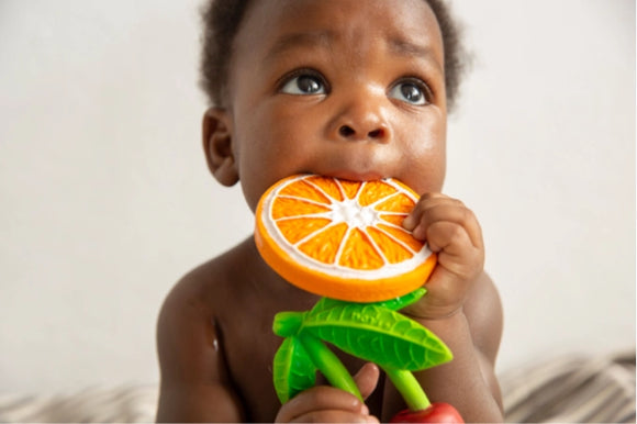 Baby holding an orange teething toy with a neutral background