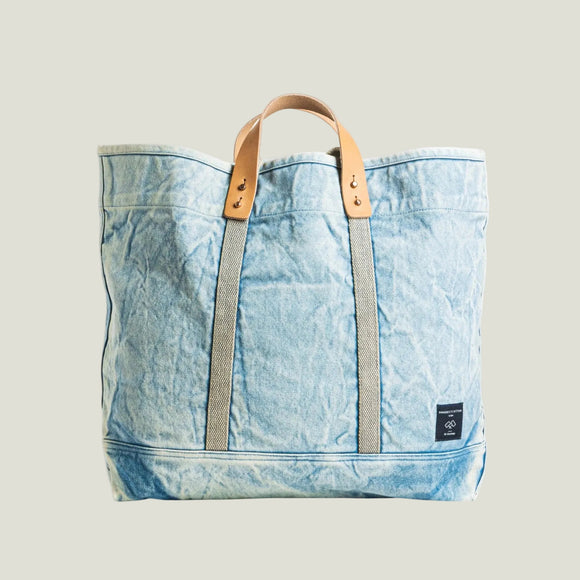 Light blue denim tote bag with brown leather straps on a white background