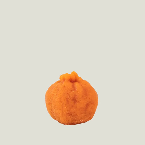 Small orange fruit wax candle on a white background.